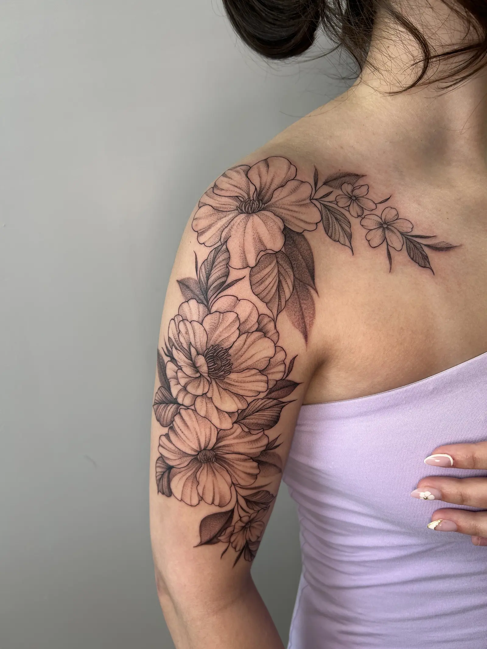 Fine-line black and grey floral tattoo of peonies and blossoms across a shoulder and upper arm